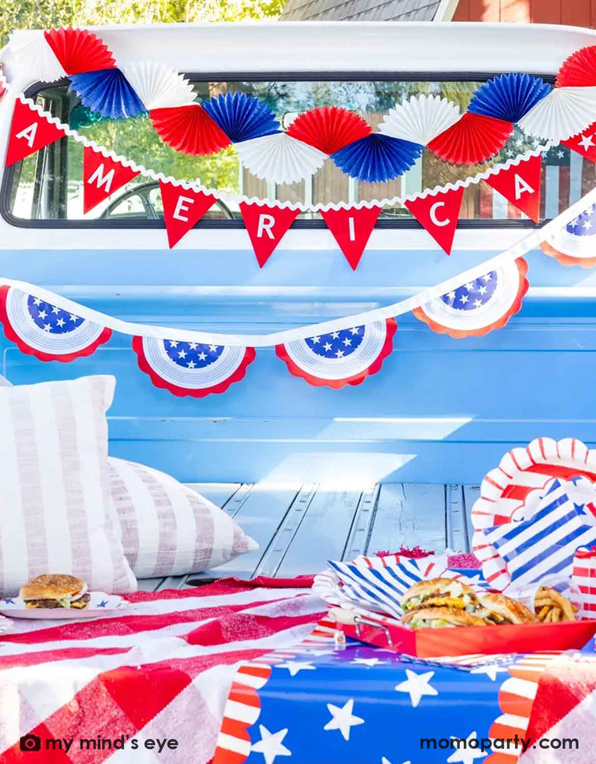 A close up shot of a light blue decorated Ford truck bed with multiple USA, American Fourth of July-themed red, white and blue decorations from Momo Party including bunting garlands, red flag banners and American flag buntings, along with various USA themed tablewares, coke bottles, burgers and fries, a perfect set up for a festive Memorial Day party or Fourth of July celebration.