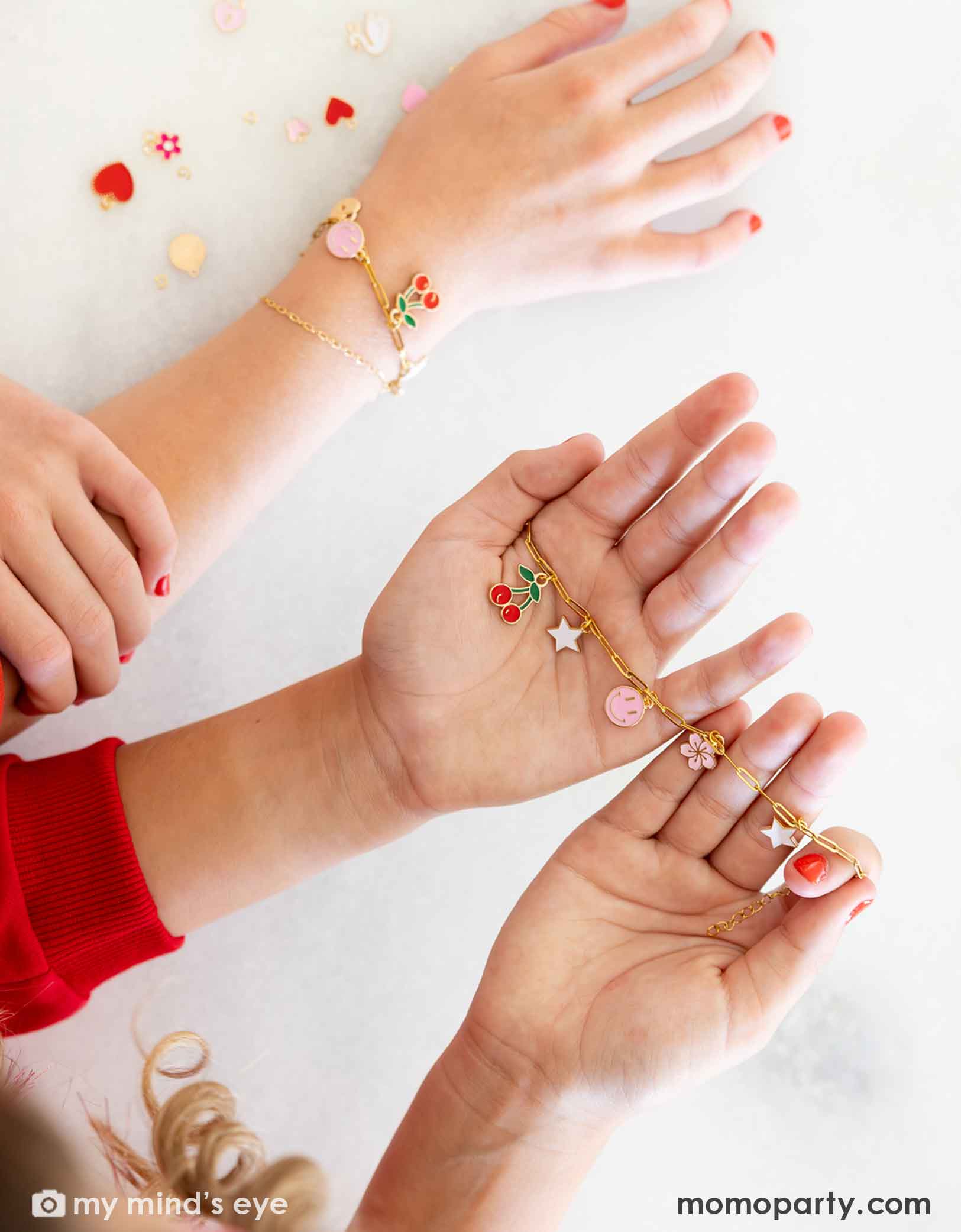 Children's hands wearing their gold bracelets with various charms from Momo Party against on a light background at a Valentine's Day themed sleep over party celebration.