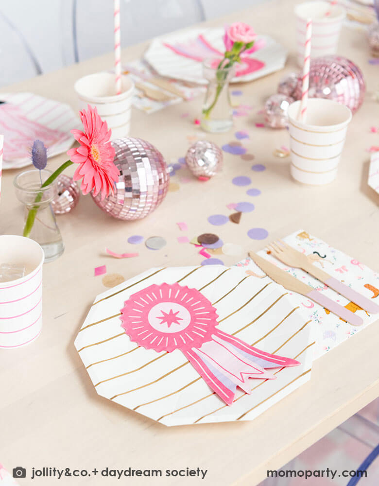 A girly pony themed party table feature Momo Party's show ribbon shaped napkins, gold striped party plates, pink striped party cups and cowgirl motif large napkins by Daydream Society. In the middle of the party table, there are some pink disco balls as the centerpiece which are with purple, pink and gold confetti spread out the table, making this an adorable inspiration for girl's derby, pony themed birthday party.