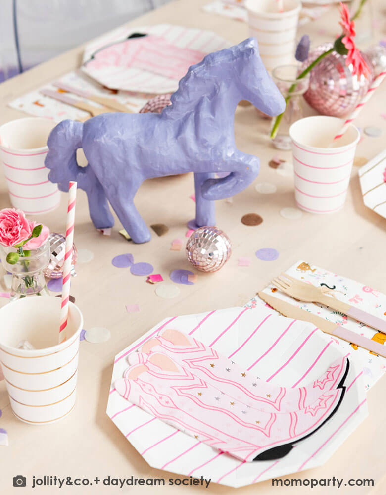 A girly cowgirl rodeo Western themed party table feature Momo Party's cowgirl boots shaped napkins, pink striped party plates, cups and cowgirl motif large napkins by Daydream Society. In the middle of the party table, there's a purple pony figure as the centerpiece which is surrounded by pink disco ball decorations, purple, pink and gold round confetti spread out the table, making this an adorable inspiration for girl's First Rodeo first birthday celebration or a cowgirl theme party for pony-loving girls!