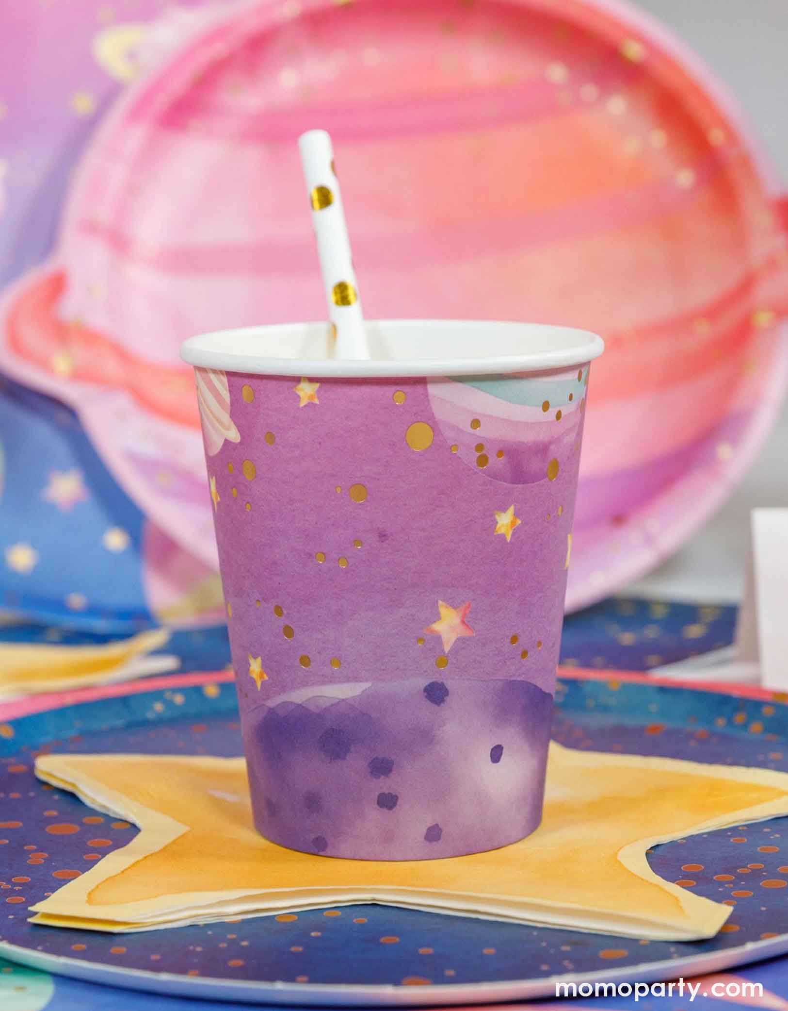 Momo Party's pink and purple ombre party cup with gold stars on a colorful space themed table setting, featuring a pink planet shaped plate, a blue galaxy themed round plate and a star shaped napkin underneath.