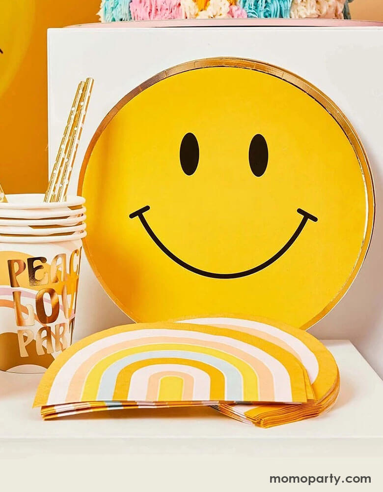 A display of Momo Party's 9" Smiley Gold Foiled Paper Plates, Peace and love retro party cups, and retro rainbow shaped napkins by Hooty Balloo. This cheery collection in the warm, retro color is perfect for any happy celebration or groovy hippie vibes themed parties.