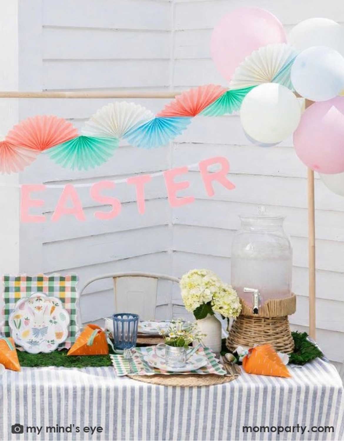An Easter-themed table setting with multiple Easter themed tablewares on the table with colorful balloons, 'Happy Easter' banner, and Momo Party's pastel tissue bunting banner decorations hung above.