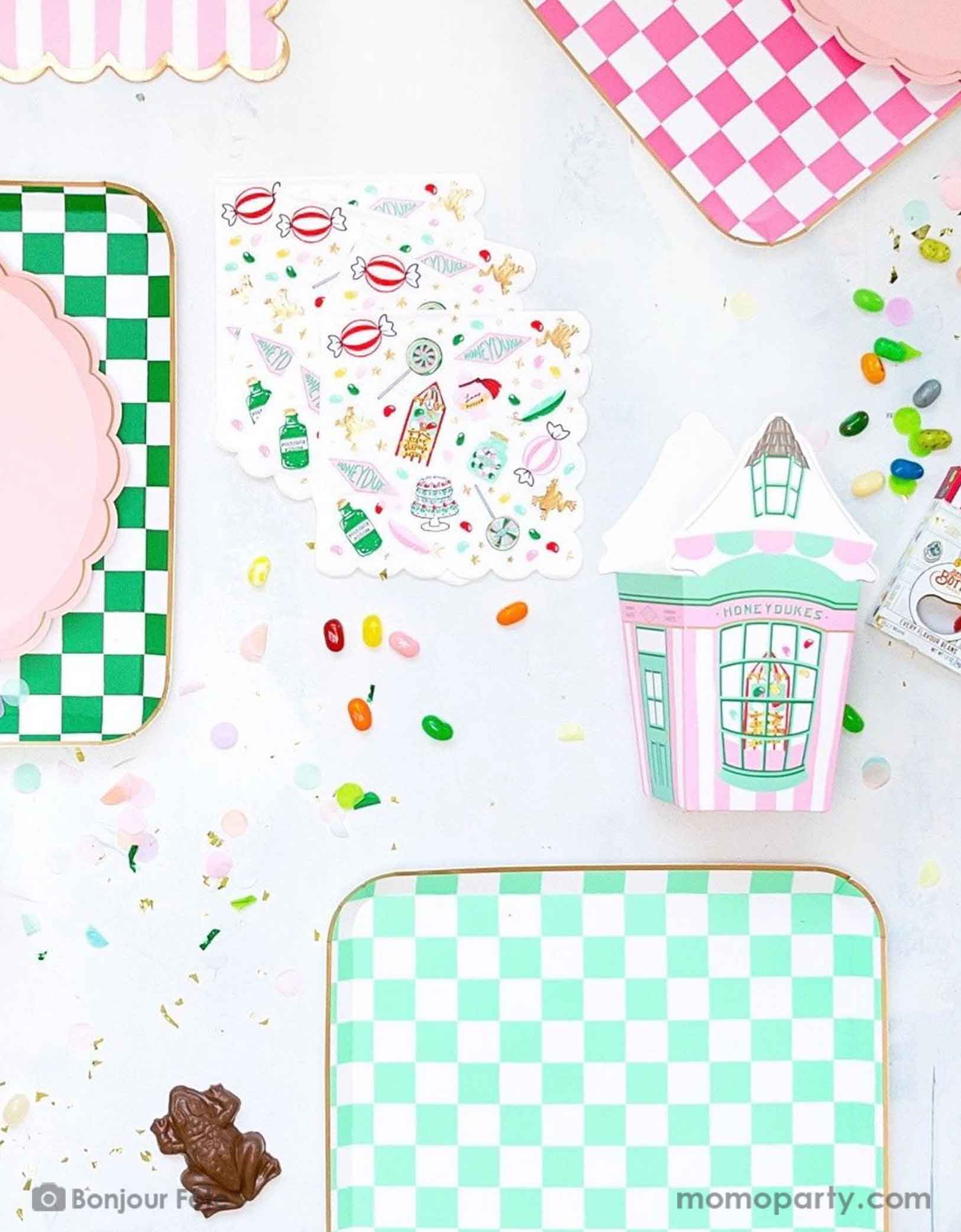 A Harry Potter themed tablescape featuring Momo Party's Harry Potter party collection including pink and green checkered dinner plates, pink striped Honeyduke large napkins, party cups and treat boxes. With chocolate frogs, Bertie Bott's Every Flavour Beans, lollipops and colorful confetti, this makes a festive scene for kid's Harry Potter themed birthday celebration.