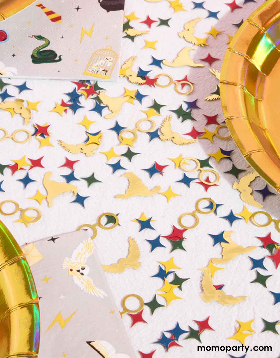 A Harry Potter themed party table featuring colorful party tableware from Momo Party along with Wizard Party Foil Confetti featuring Harry Potter themed designs including starburst in red, green, yellow and red, glasses, sorting hats and owls scattered around on a white party table.
