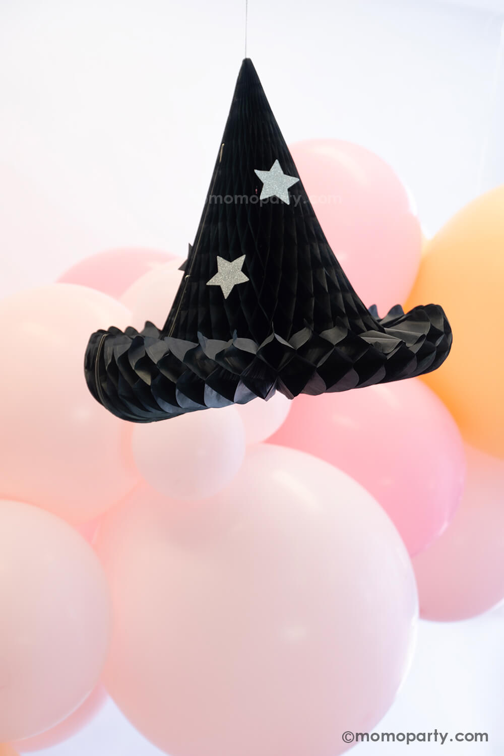 Momo Party's Hocus Pocus Witch Hat Honeycomb decoration hung next to an adorable pink balloon garland with various sized balloons in pastel pink, pink and blush colors. This makes a great decoration for a sweet girly pink Halloween that's perfect for this spooky season.