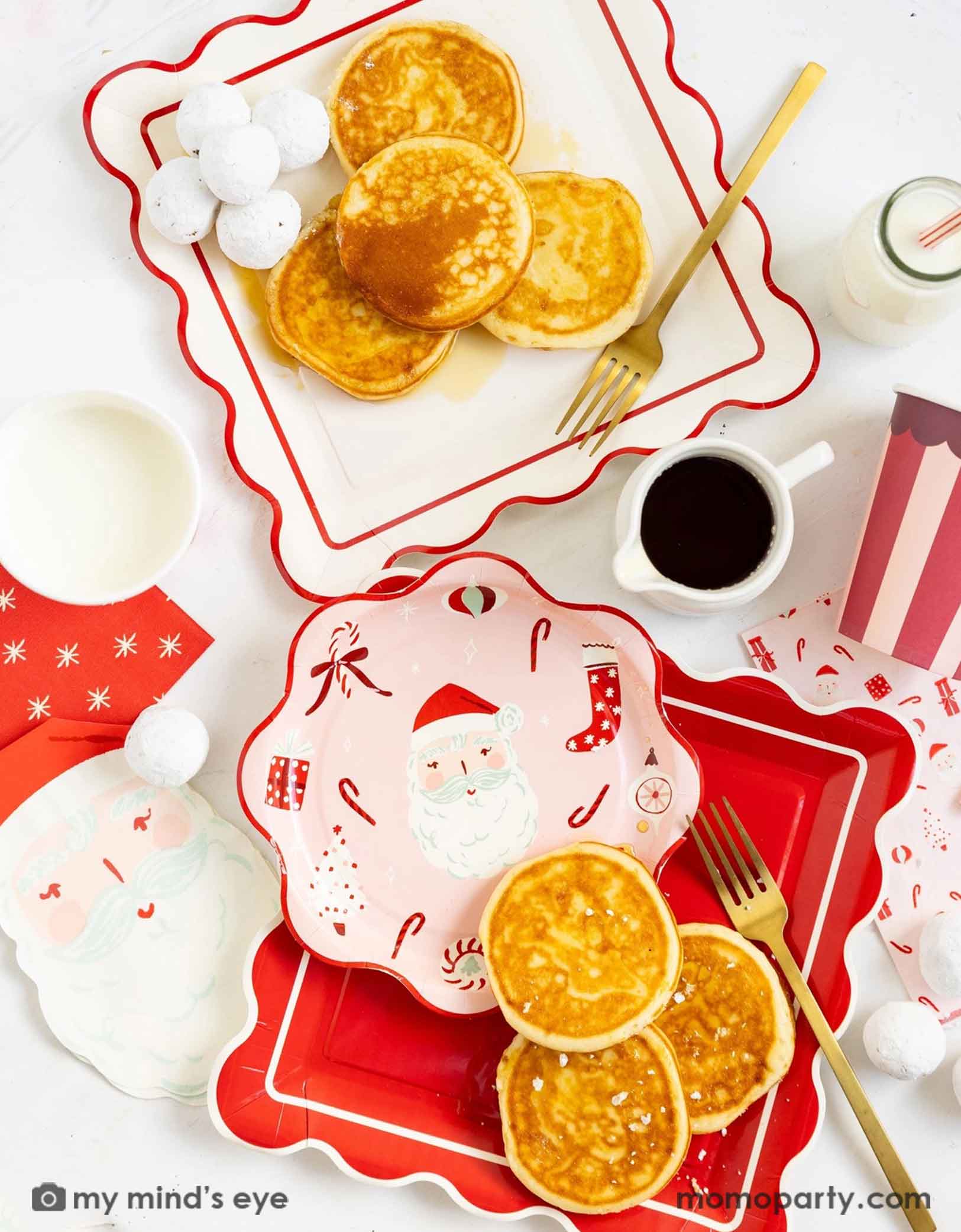 A festive Christmas breakfast scene with pancakes, milk, coffee, and Momo Party's Dear Santa party collection including the scallop square plates in red and cream, scallop round table with Santa and candy cane designs, Santa shaped napkins and red striped party cups on a white table.