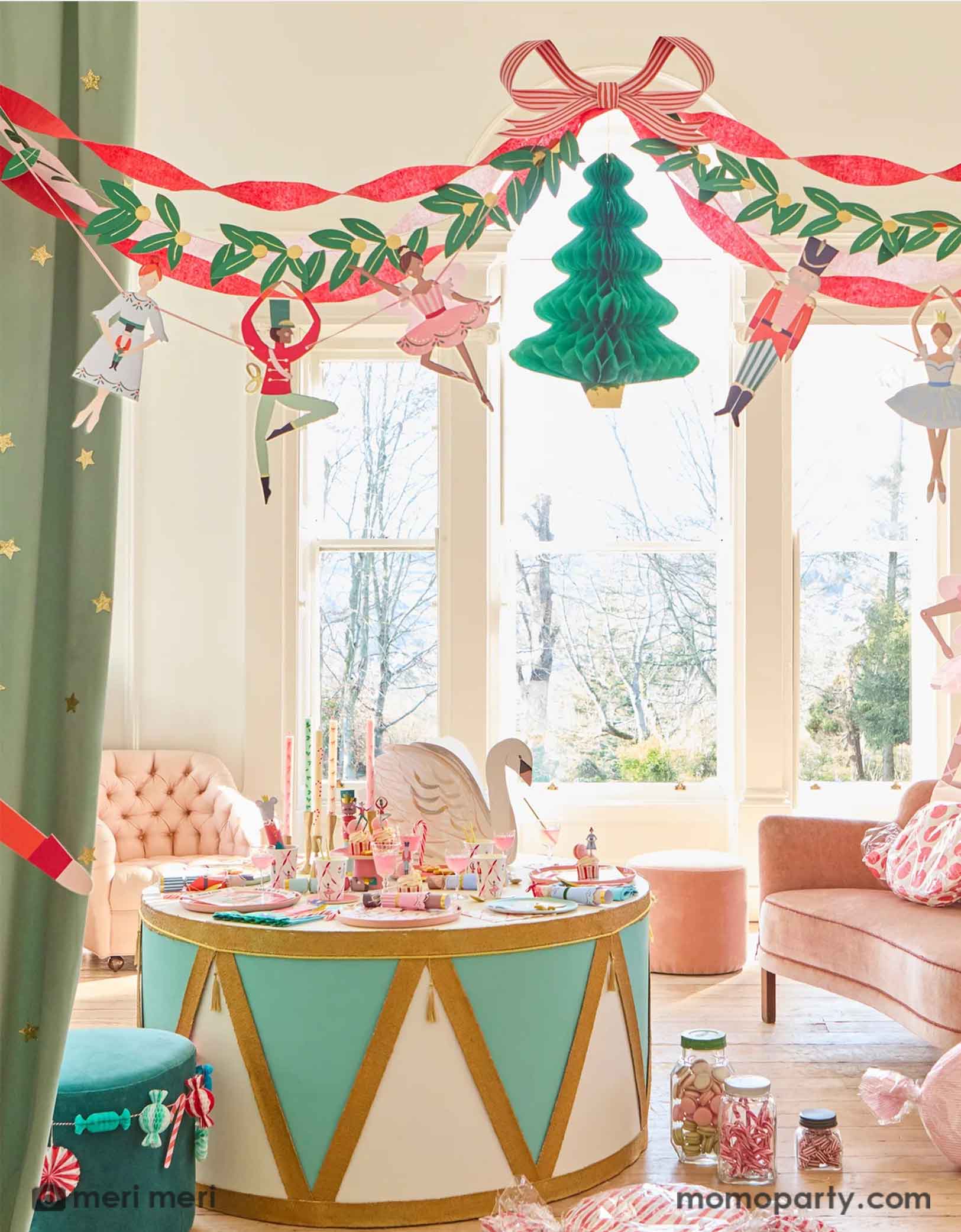 A festive children's room decorated with multiple Christmas themed decorations from Momo Party including a Nutcracker drum shaped table with Nutcracker themed party tablewares of plates, napkins, party cups and centerpiece. On the floor there are some candy jars with peppermint candies. Above the table hung the festive Nutcracker Ballet Garland featuring Nutcracker's characters including ballerina, the Mouse King, soldiers, and ribbons, making this a great inspiration for a sweet Holiday celebration.