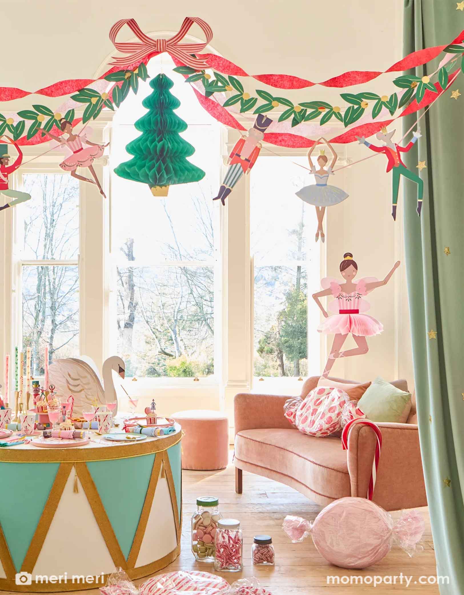 A festive children's room decorated with multiple Christmas themed decorations from Momo Party including a Nutcracker drum shaped table with Nutcracker themed party tablewares of plates, napkins, party cups and centerpiece. On the floor there are some candy jars with peppermint candies. Above the table hung the festive Nutcracker Ballet Garland featuring Nutcracker's characters including ballerina, the Mouse King, soldiers, and ribbons, making this a great inspiration for a sweet Holiday celebration.