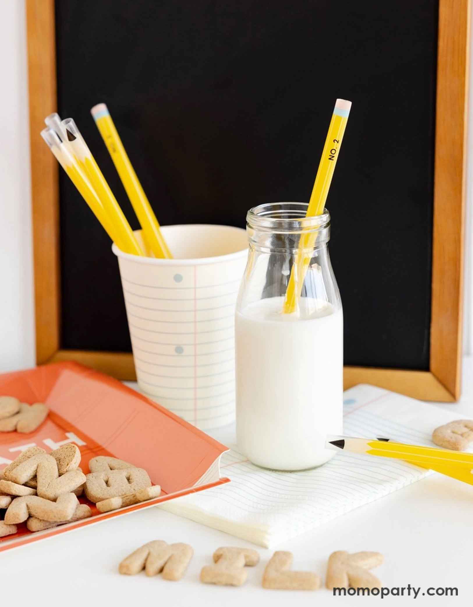 A clean and modern breakfast table featuring Momo Party's school themed party supplies including the 8oz notebook party cup with pencil shaped reusable straws, a stack of notebook paper guest napkins and a classic milk bottle filled with milk. On the table there are some alphabet cookies spelling out MILK and a small chalkboard in the back, making it a perfect info for first day of school breakfast set up for kids!