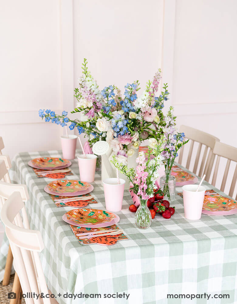 A cute kid's bug insect themed party table set up featuring Momo Party's backyard bug patterned plates, napkins paired with pink party cups and plates. With an olive green gingham tablecloth under and beautiful flower bouquets, this makes a perfect inspiration for a modern take of a kid's bug themed celebration.