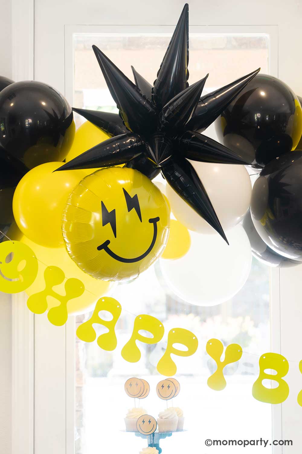 Kid's "Cool Dude" themed Party Balloon Garland decoration by Momo Party featuring retro neon happy birthday banner with a balloon garlands in black, white and yellow adorned with a black starburst foil balloon and smiley fact foil balloon with lightning bolt eyes. This decoration is perfect for boy's "One Happy Dude" themed first birthday, a "Two Cool" themed second birthday party or "Ten Rad Years" 10th birthday party.