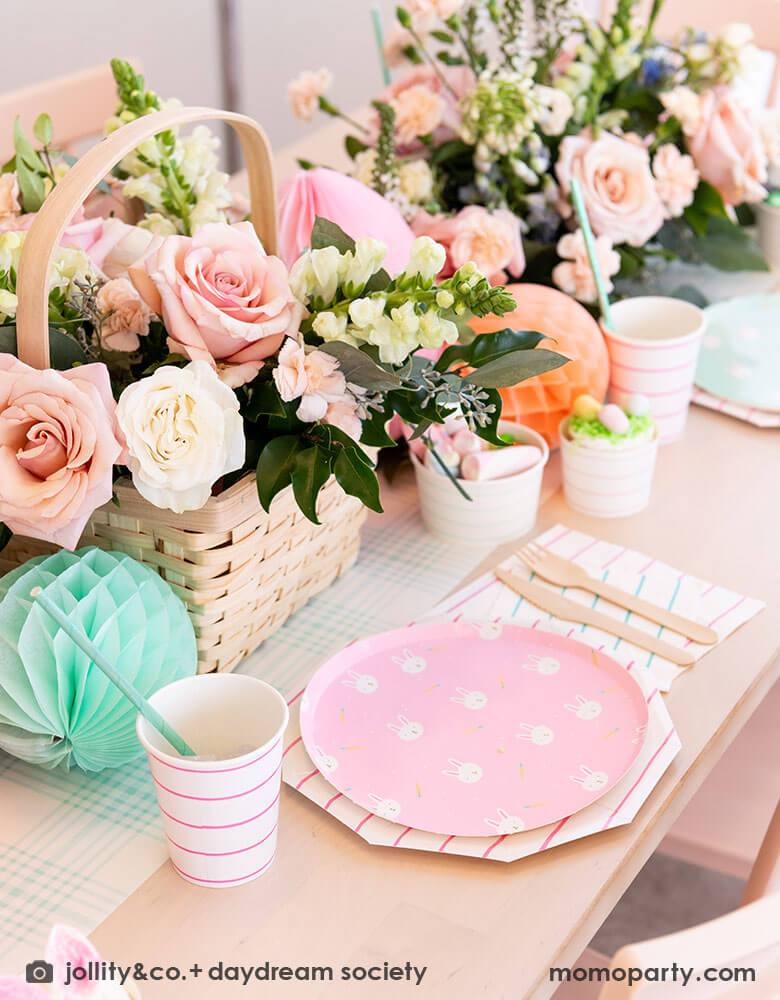 A beautiful Easter brunch table features Momo Party's Easter fun small plates along with striped party plates, cups, and napkins. In the middle of the table lays a blue gingham table runner which has baskets of spring flower arrangement and egg shaped honeycomb decorations in pastel colors, making this an adorable inspo for a Easter party tablesetting.