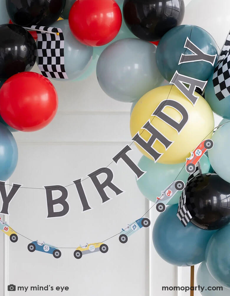 A kid's race car themed birthday party decoration set up features Momo Party's 4ft & 6ft Miles Per Hour race car happy birthday banner set, a balloon garland in dark blue, light blue, gray, red and black colors adorned with checkered race car flags, making this a perfect inspo for modern kid's car themed parties, be it a "Fast One" first birthday party, a "Two Fast" second birthday party, "speed limit 3" or "grand 3" third birthday or a "Need Four Speed" fourth birthday bash.