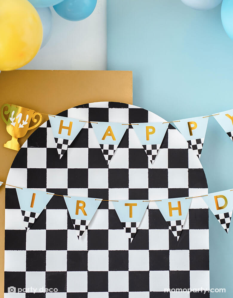 A close up of a race car checkered party backdrop adorned with Momo Party's trophy race car happy birthday banner - This banner celebrates the big day with "Happy Birthday" written on it with trophy pennants.
