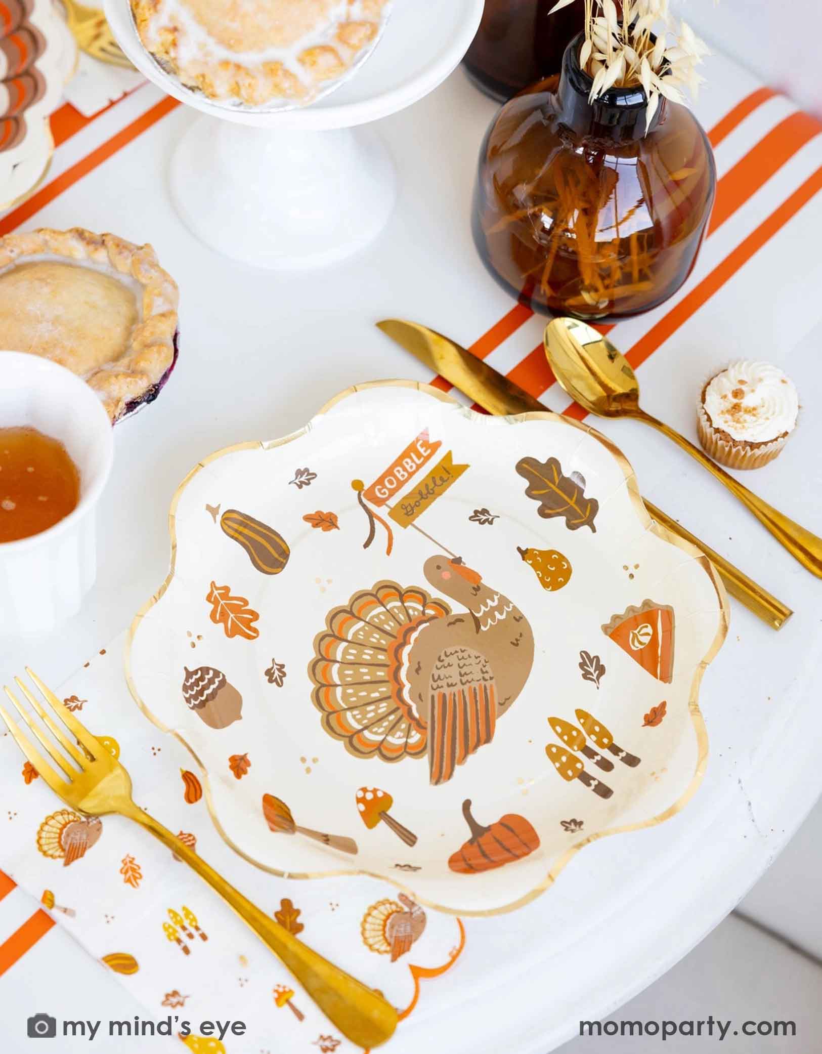 A Thanksgiving-themed party table featuring various Thanksgiving themed party supplies from Momo Party including turkey plates, napkins, gold cutlery, orange striped table runner, party cups with fall themed designs on them. With decorative elements and fall themed desserts and pumpkin pies on a table.