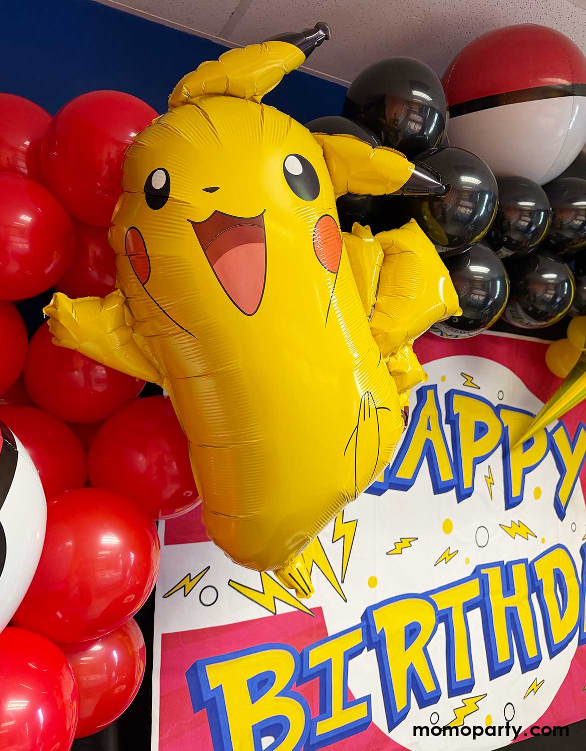 A kid's Pokemon themed birthday party decoration by Momo Party featuring Yellow Pikachu shaped foil balloon among red, black, and yellow latex balloon garland and pokeball foil balloons with a matching 'Happy Birthday' banner sign.