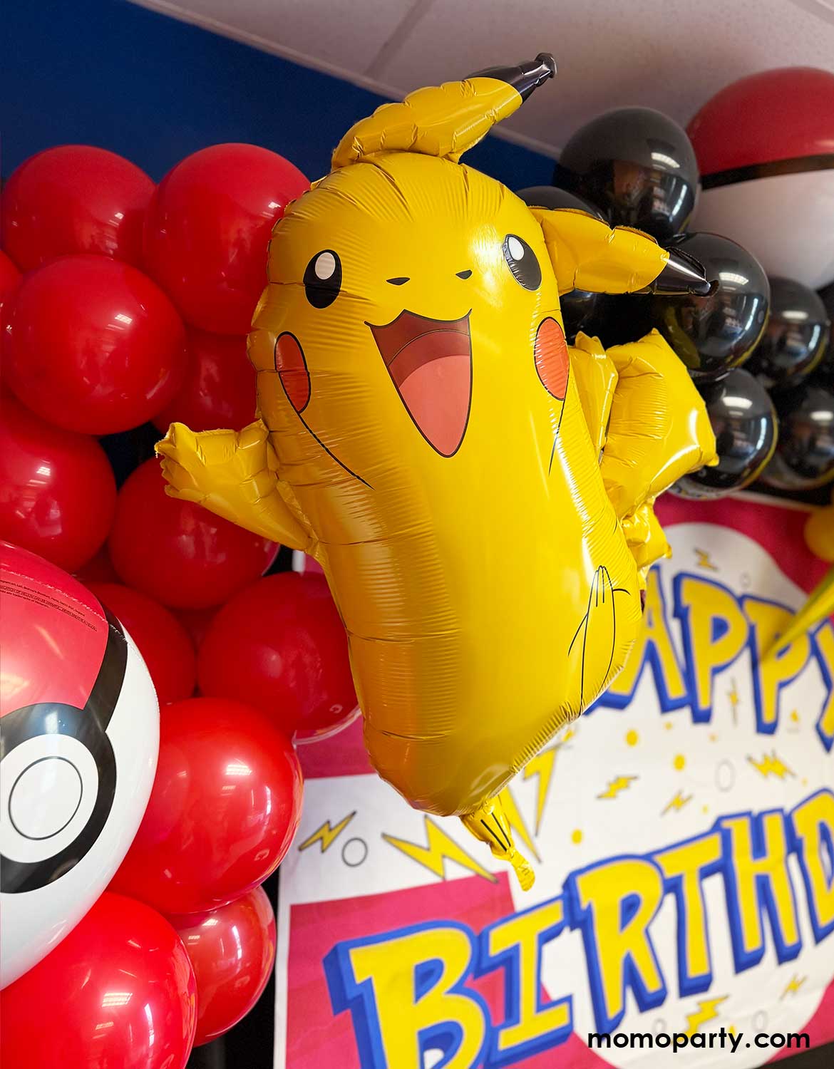 A kid's Pokemon themed birthday party decoration by Momo Party featuring Yellow Pikachu shaped foil balloon among red, black, and yellow latex balloon garland and pokeball foil balloons with a 'Happy Birthday' banner sign.