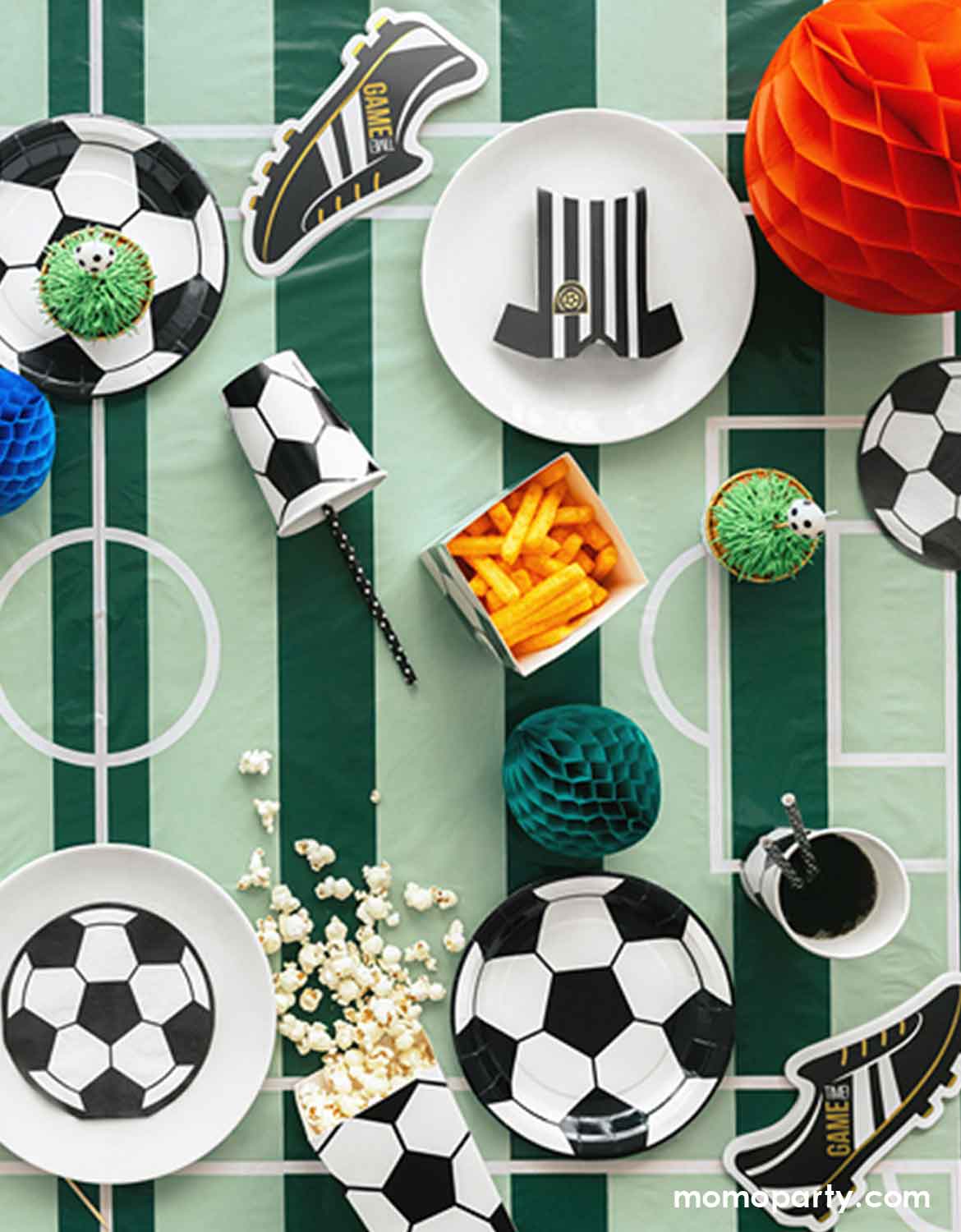 Soccer-themed party table setting with plates, cups, and decorations on soccer field tablecloth from Momo Party.