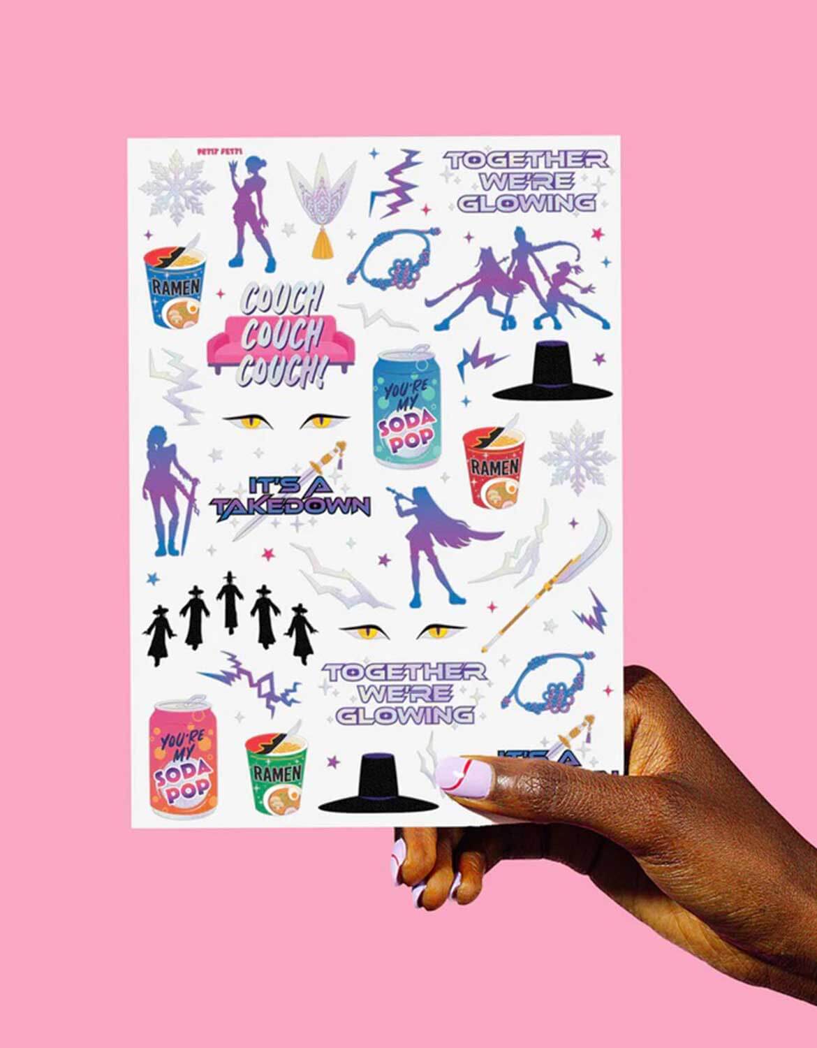 Momo Party's Kpop Demon Hunters themed temporary tattoo sheet with colorful graphics including dancing figures, soda pop cans, lightning power symbols and texts by Xo, Fetti held by a hand against a pink background