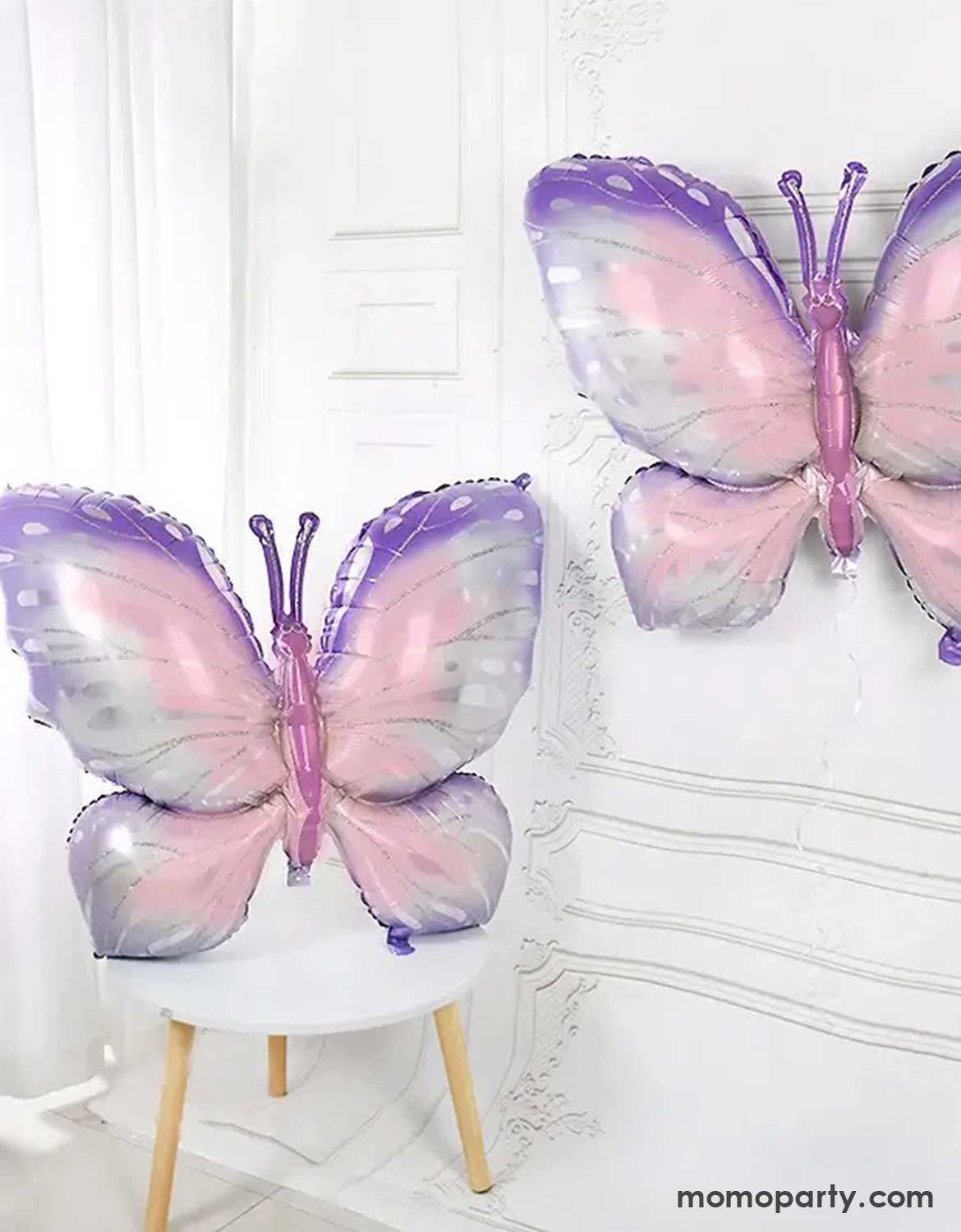 Momo Party's 39" Butterfly-shaped balloons in pink and purple on a white chair against a white wall.