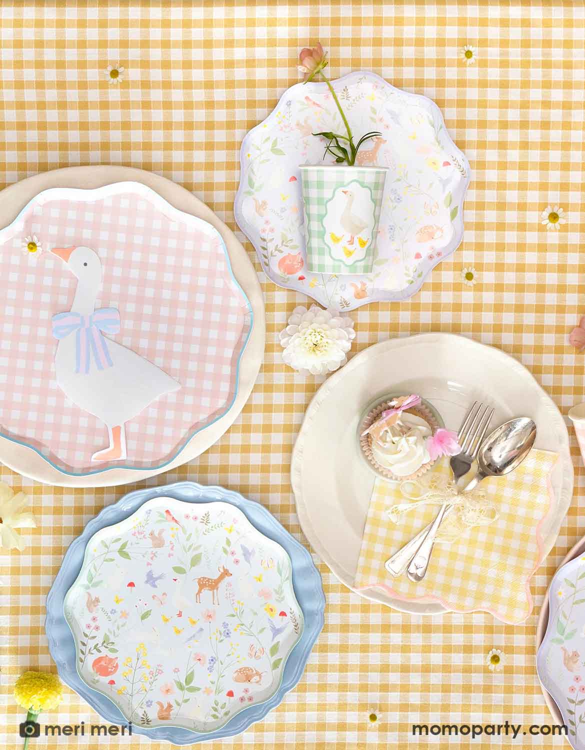 An overhead shot of a party table featuring Momo Party's gingham checkered plates and little animals plates, along with goose shaped napkins and party cup on a yellow gingham checkered tablecloth. A perfect setting for a cottage-inspired celebration, be it a kid's first birthday party, a baby shower or an Easter celebration.