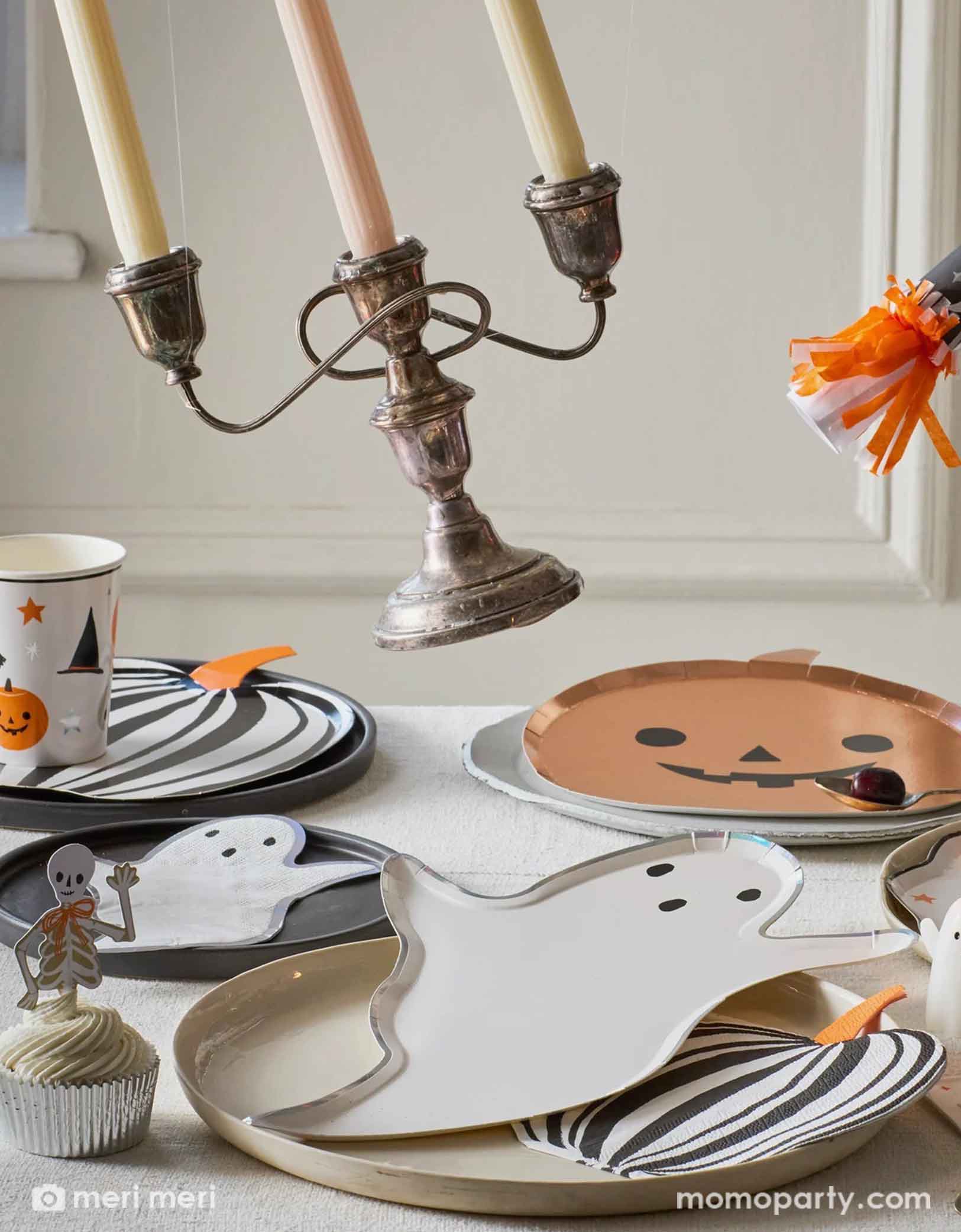 A Halloween-themed table setting with an array of Momo Party's Halloween party supplies including Halloween party cups, ghost and pumpkin shaped plates and matching napkins, black striped pumpkin plates and napkins by Meri Meri. With ghost candles, Halloween ghost party crackers and decorative items flying off on the table, this creates a fun scene for a kid's friendly Halloween celebration in this spooky season!