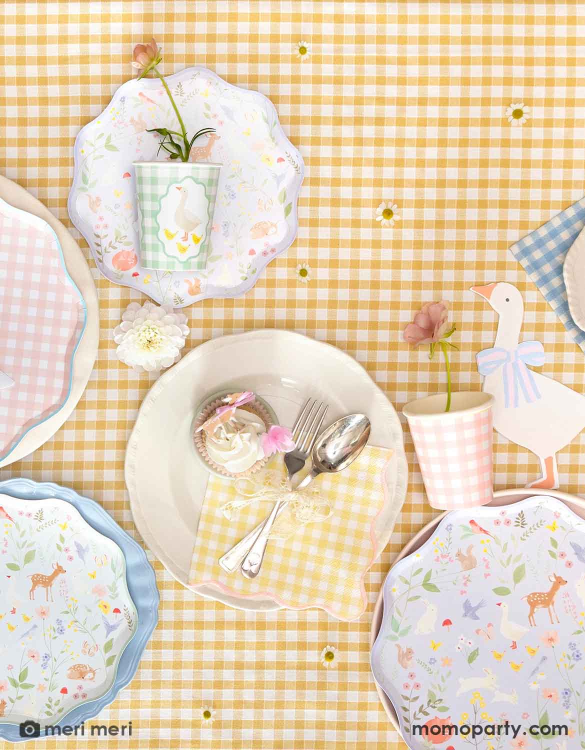 An overhead shot of a party table featuring Momo Party's gingham checkered plates and little animals plates, along with goose shaped napkins and party cups on a yellow gingham checkered tablecloth. A perfect setting for a cottage-inspired celebration, be it a kid's first birthday party, a baby shower or an Easter celebration.