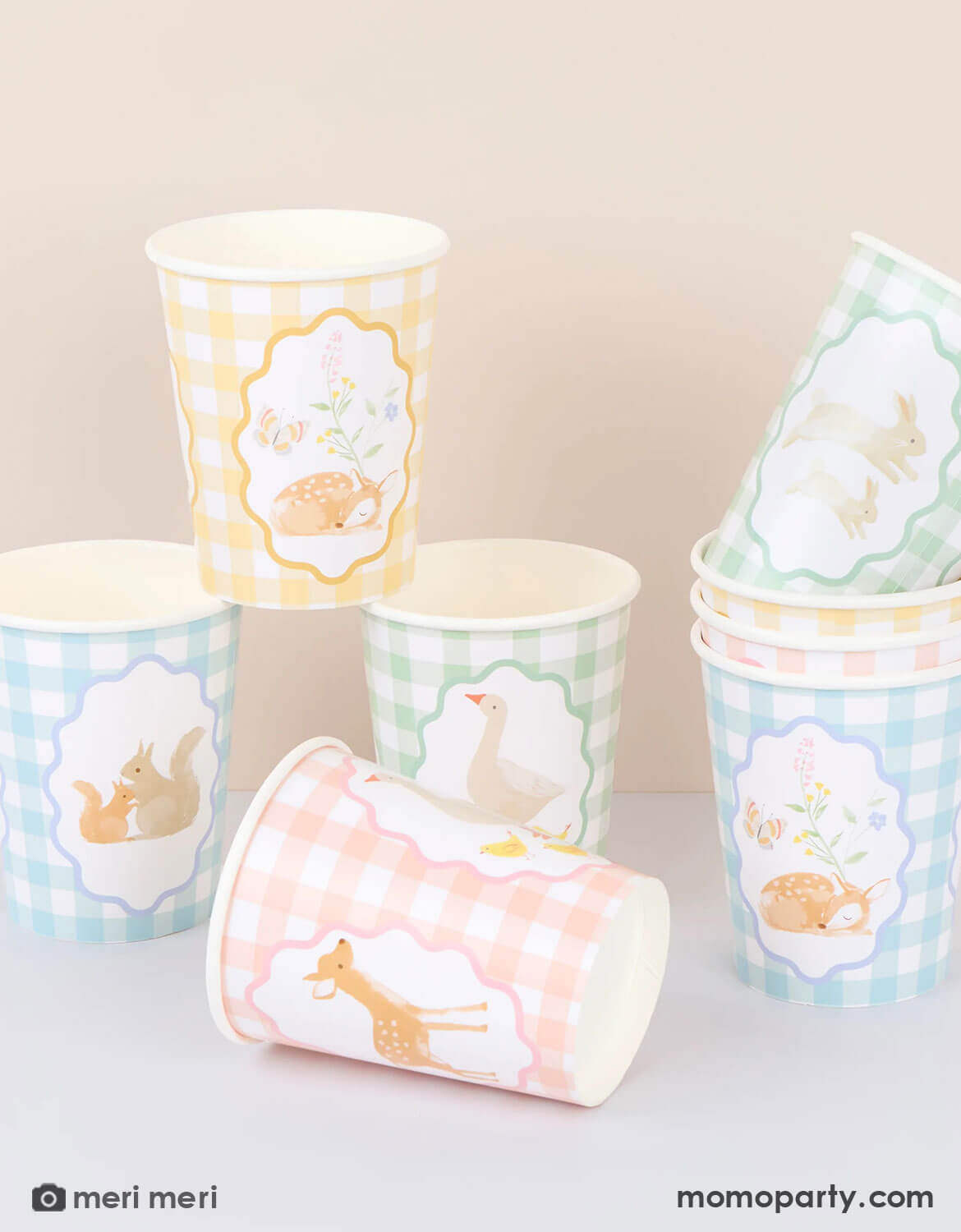 A set of Momo Party's gingham paper cups with rustic little animal illustrations in soft pastel colors stacked on a beige background.