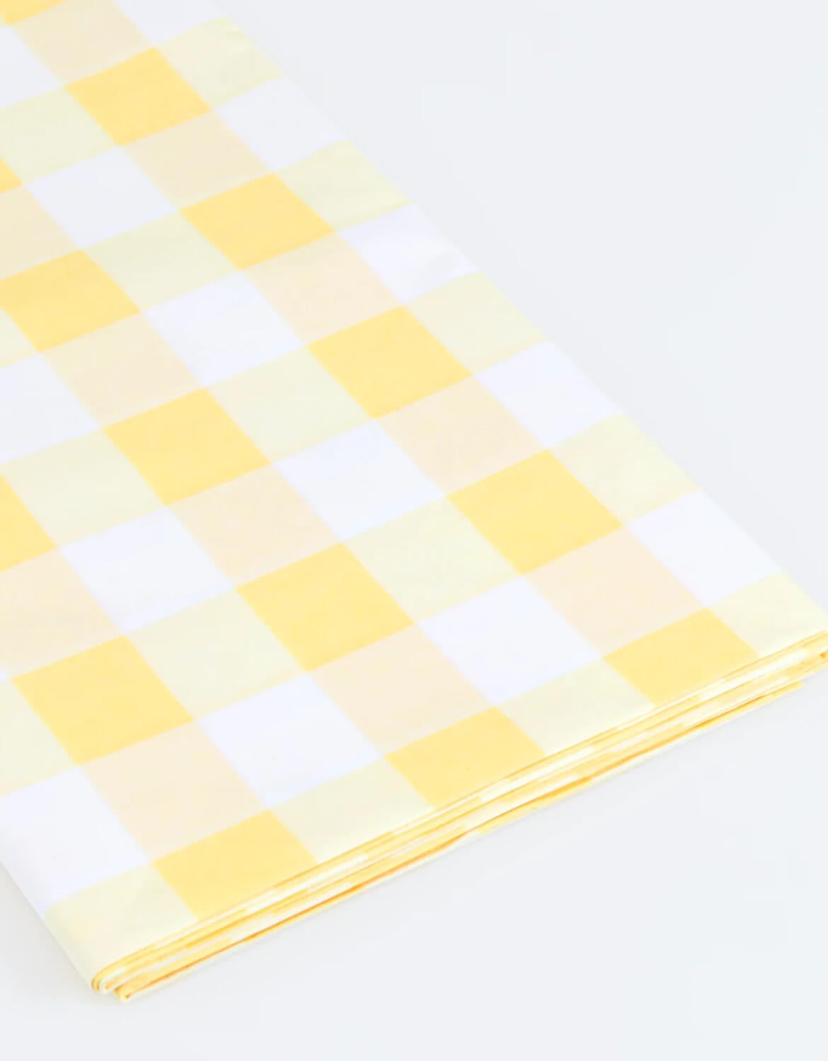 A close up shot of Momo Party's paper tablecloth with yellow and white checkered design by Meri Meri on a white background.