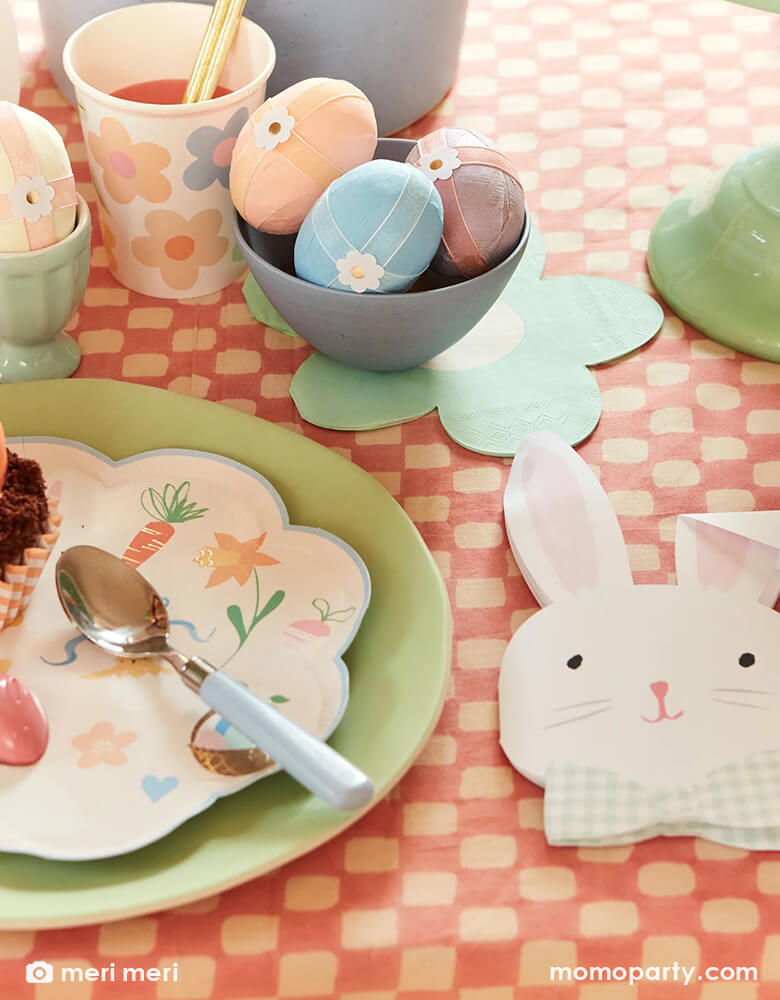 An Easter party table with Easter eggs adorned with Meri Meri's Easter themed tattoo stickers, on the table are Momo Party's Easter themed plates and napkins in soft pastel colors including bunny shaped napkins which are coordinated with the charming daisy shaped napkins, makes this an adorable tablescape idea for a spring gathering.