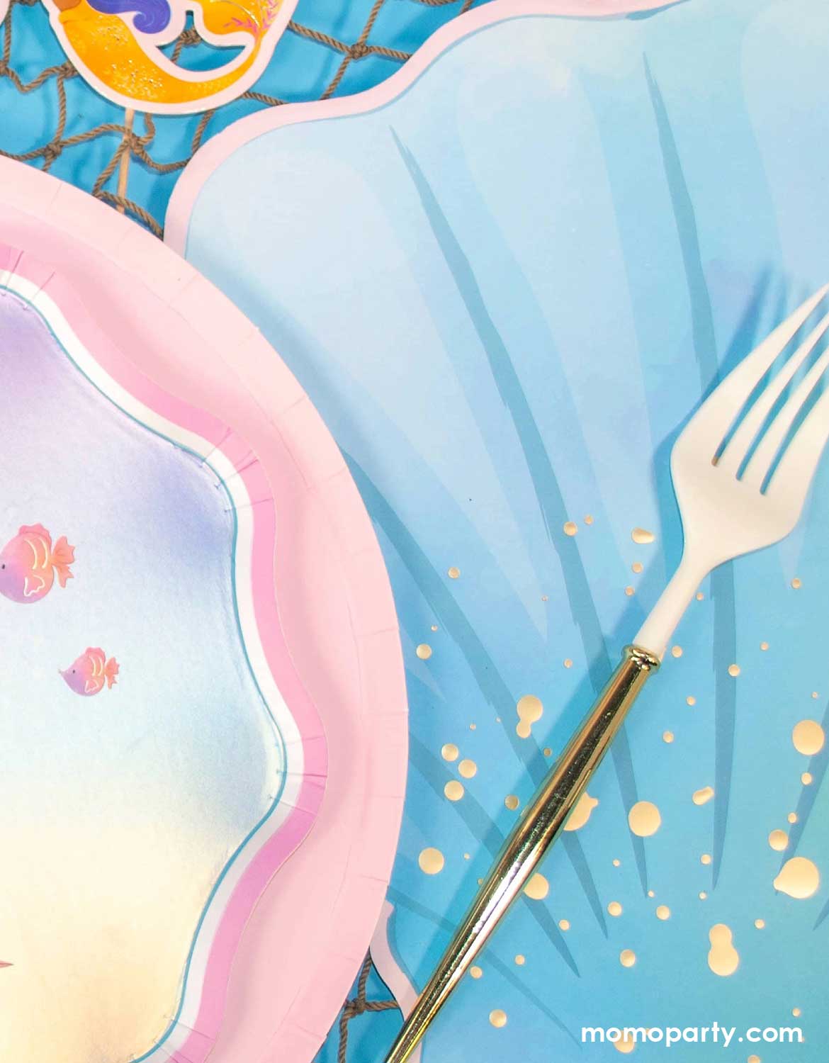 Colorful pastel plates with a gold fork on Momo Party's ocean blue placemat with golden speckles.