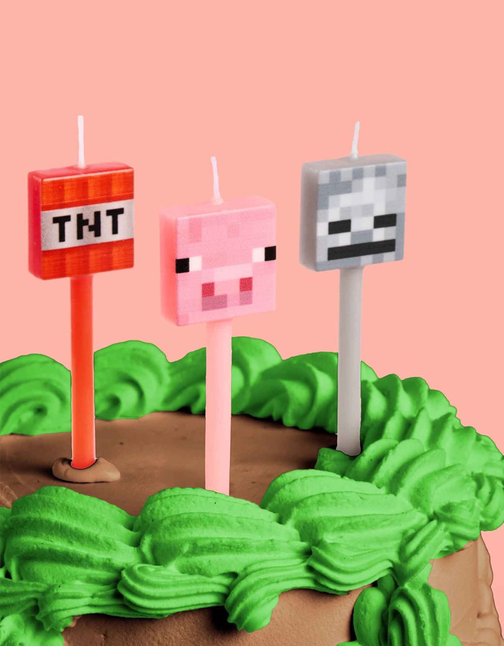 A close up of a Minecraft themed birthday cake with brown and green buttercream topped with three Momo Party's Pixel Minecraft Candles featuring TNT, pig face, and a pixel face.