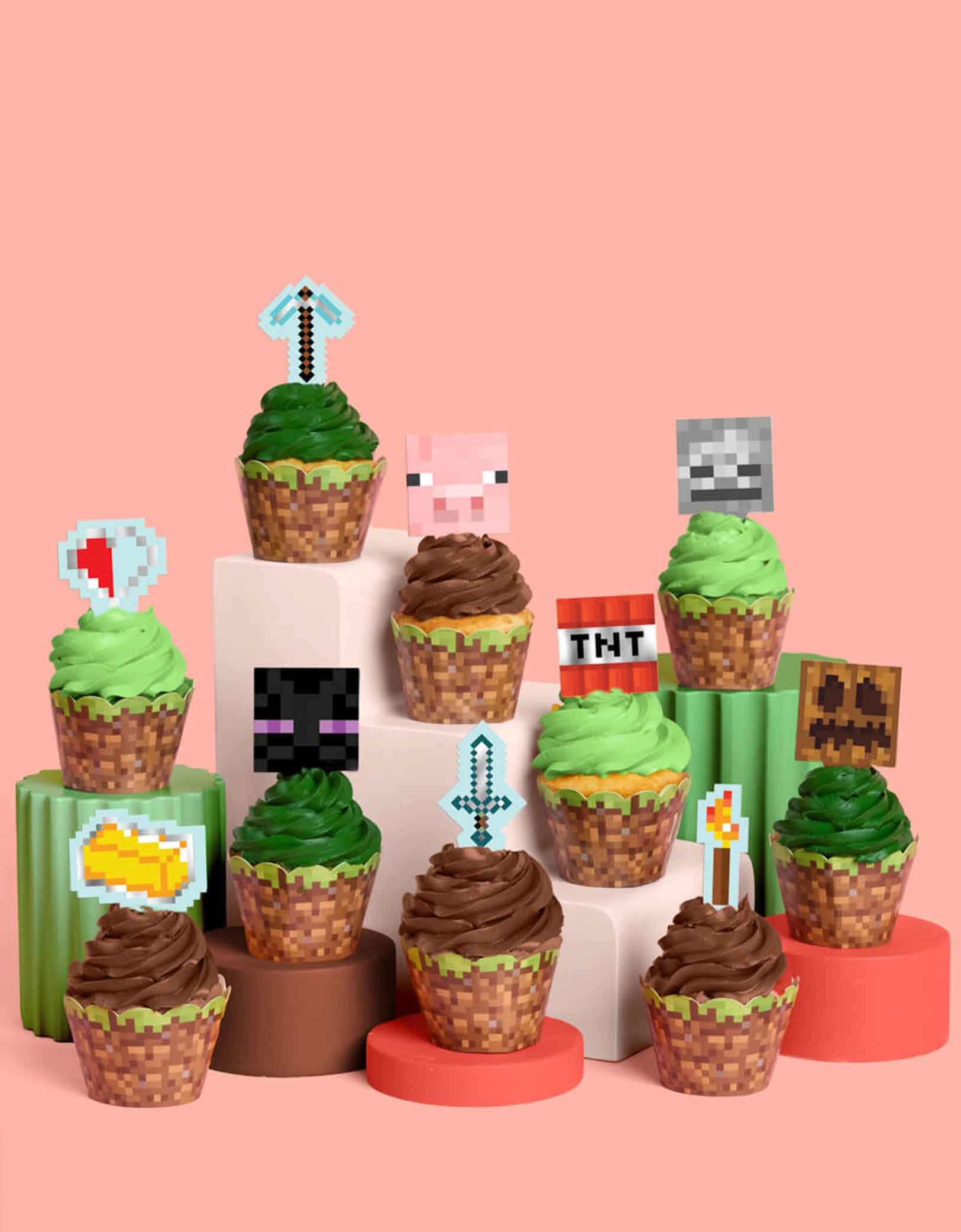 A set of Minecraft-themed cupcakes in green and brown with decorative Minecraft themed toppers and liners featuring pig face, pixel swords, Enderman, pixel faces, TNT, gold bricks etc from Momo Party on a pink background.