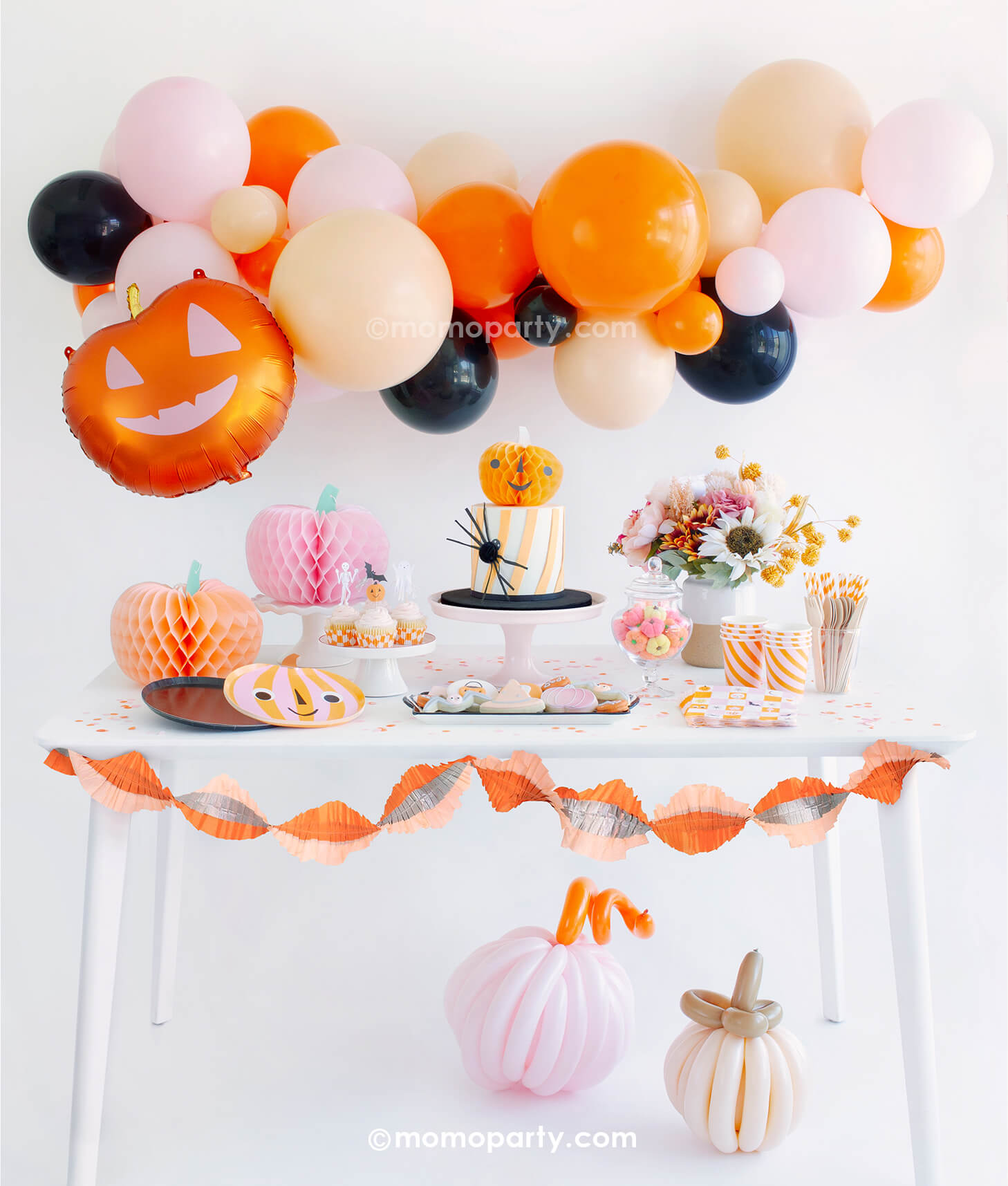 Momo Party's "Hey Pumpkin" Halloween party box featuring adorable pumpkin themed party supplies including a boo-tiful balloon garland in orange, pink, blush and black colors, smiley pumpkin shaped plates, groovy Halloween checkered napkins, honeycomb pumpkin decorations in pink and peach colors, with the pink and orange crepe streamer hung around the table and two boho colored pumpkin made with twisting balloons, this party look is perfect for a girly, kid's friendly pink Halloween bash this season! 