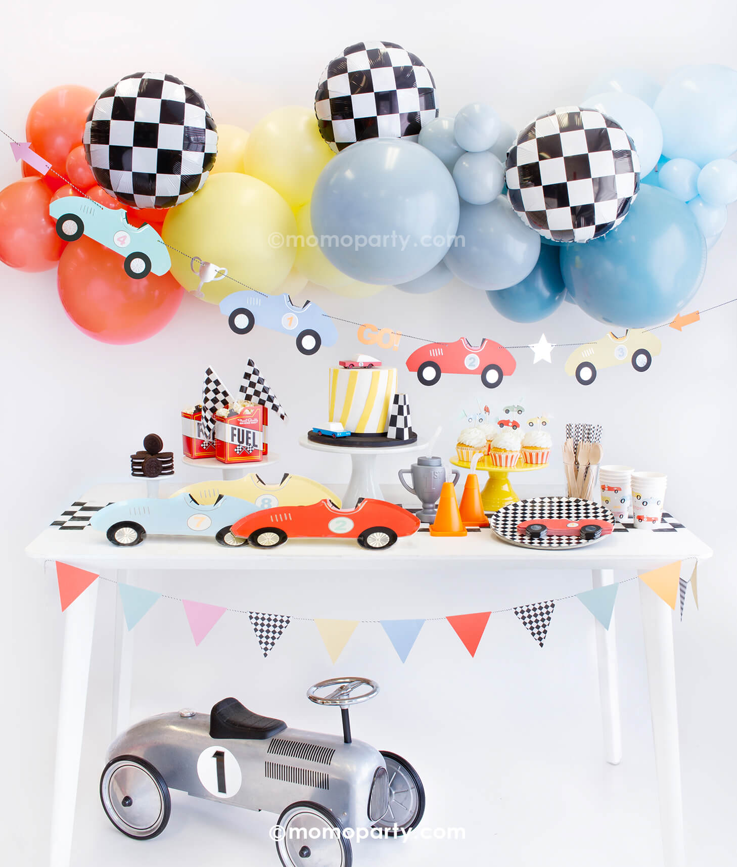 Momo Party Race Car Box, set up inspiration with Meri Meri race car paper plates, race car shape napkins, race car graphic party paper cups, checkered round side plates, neon confetti flag cupcake kit, candy car as cake topper, Fuel treat favor box with popcorns as tableware, colorful balloon cloud, race car party garland with party pennants in pastel colors, checkerboard foil balloon as decorations for modern Race car, car themed "Two Fast" second birthday party or a "Fast One" first birthday party.