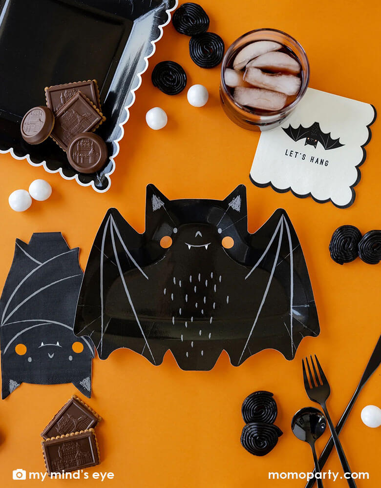 A classic Halloween black and orange table featuring Momo Party's 10.5" x 8.5" bat shaped plates, napkins and black square plates with white scalloped edge. Along the tableware, there are some black and white Halloween treats including candies, chocolates and gum balls, makes it a great party inspiration for kid's friendly Halloween party ideas.