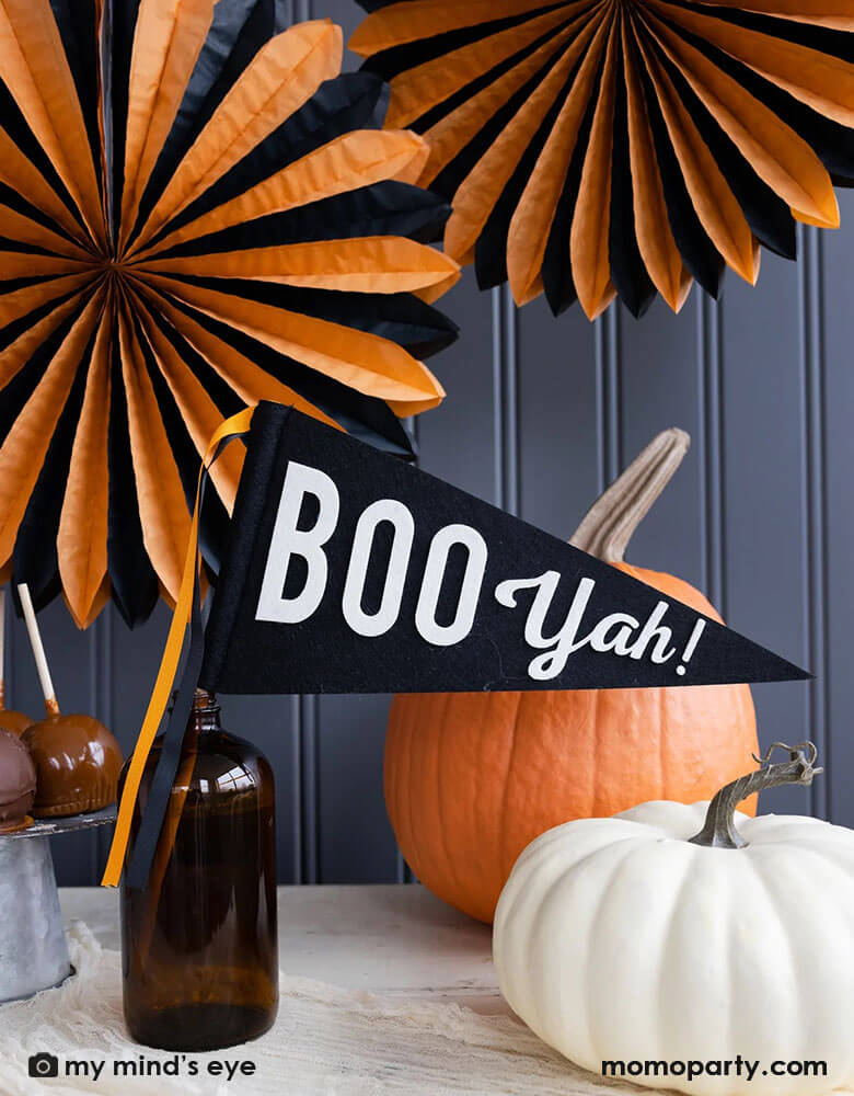 A classic orange and black Halloween table decorated with pumpkins, caramel apples and Momo Party's 14" x 15" Boo Yah black and white felt party pennant with orange and black ribbons. In the back the wall was decorated with My Mind's Eye's oversized orange and black tissue paper fans. All makes a simply yet iconic Halloween decorating inspo this Halloween season. 