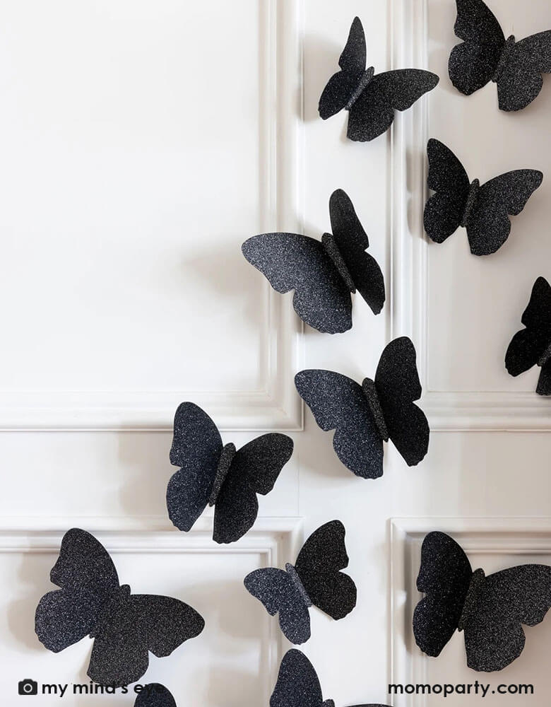 A close up of a white wall decorated with Momo Party's black glitter butterfly wall decorations by My Mind's Eye.