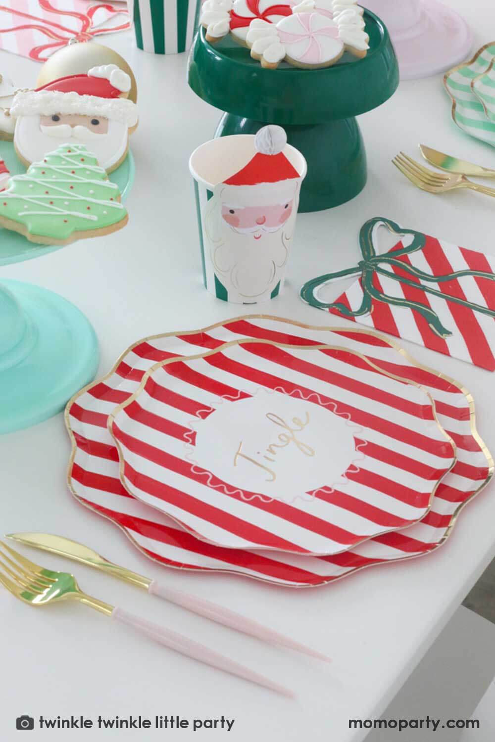 A festive Christmas party table featuring Momo Party's Festive striped dinner plates, side plates, present with a bow shaped napkins and Christmas honeycomb party cups in Santa design by Meri Meri. In the center of the table are a mint and green cake stand with festive Holiday cookies in the design of Peppermint, Santa, Christmas tree, candy cane and snowflake. Makes this a modern inspo for a festive Holiday table setting.