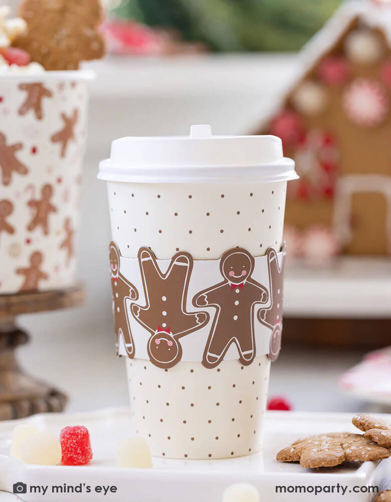 A gingerbread house decoration party featuring Momo Party's 16 oz Ginger Dots To-Go Cups by My Mind's Eye. On the back you can see a gingerbread house decorated with peppermint and candies, plus a treat bucket with gingerbread man pattern design filled with gingerbread cookies.
