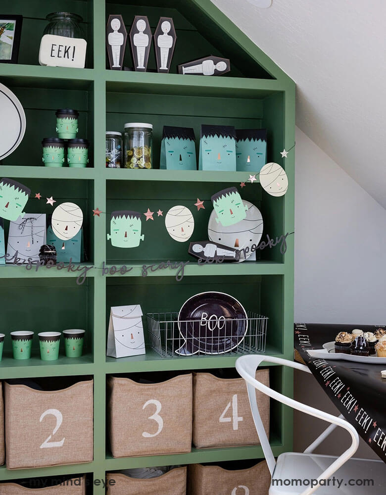 A green shelf filled with Momo Party's Frank & Mummy party supplies by My Mind's Eye. Including Frankenstein plates, cups and gift bags, plus the black boo plates. It's perfect for boy's Halloween party!