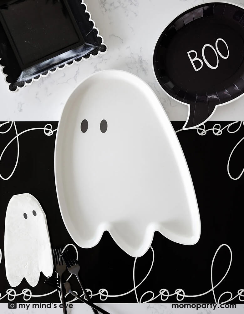 A black and white Halloween table featuring Momo Party's 12" x 16" ghost shaped bamboo reusable tray. Around it it's the black boo shaped plates, ghost shaped napkins on a black table runner with "boo" scripted font written over it. All makes a cool and spooky ideas for a kid's Halloween bash, trick or treat party, or Halloween theme birthday party table setting inspiration.