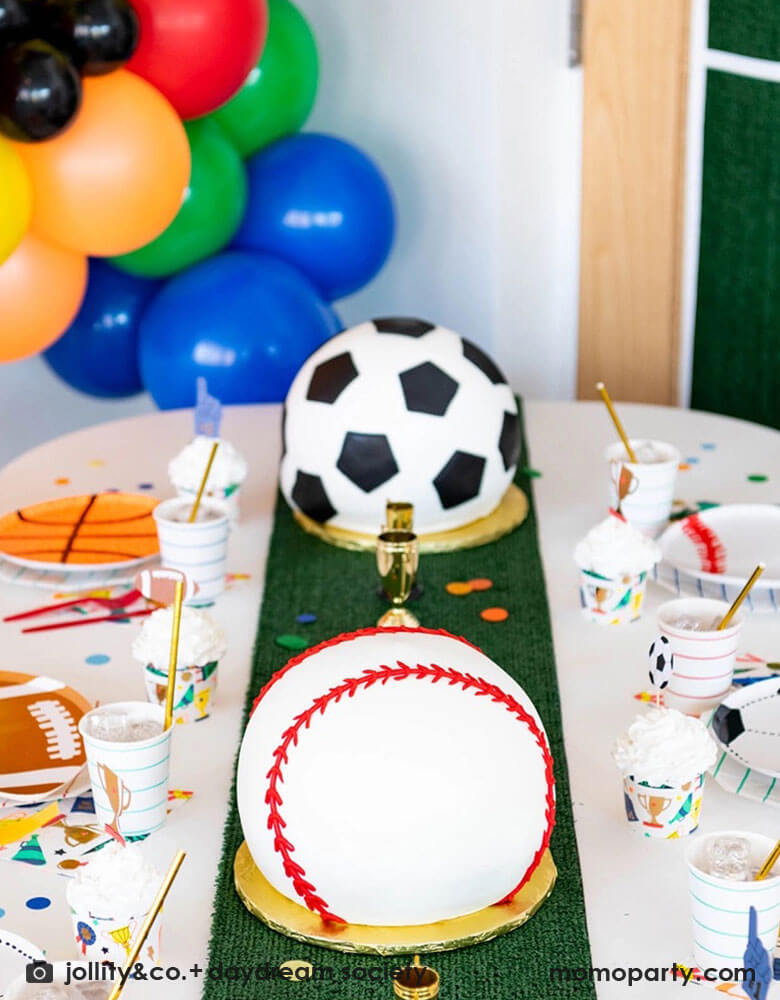 A fun sports themed party table filled with Momo Party's sports themed party tableware including soccer ball, football, baseball, basketball shaped plates, football shaped plates, basketball shaped plates with mint and red striped plates and cups, plus some good sport large napkins featuring bright colors and fun illustrations of sports elements. In the center of the table there's a faux grass table runner and baseball shaped birthday cake, all makes great inspirations for kid's sport themed parties.