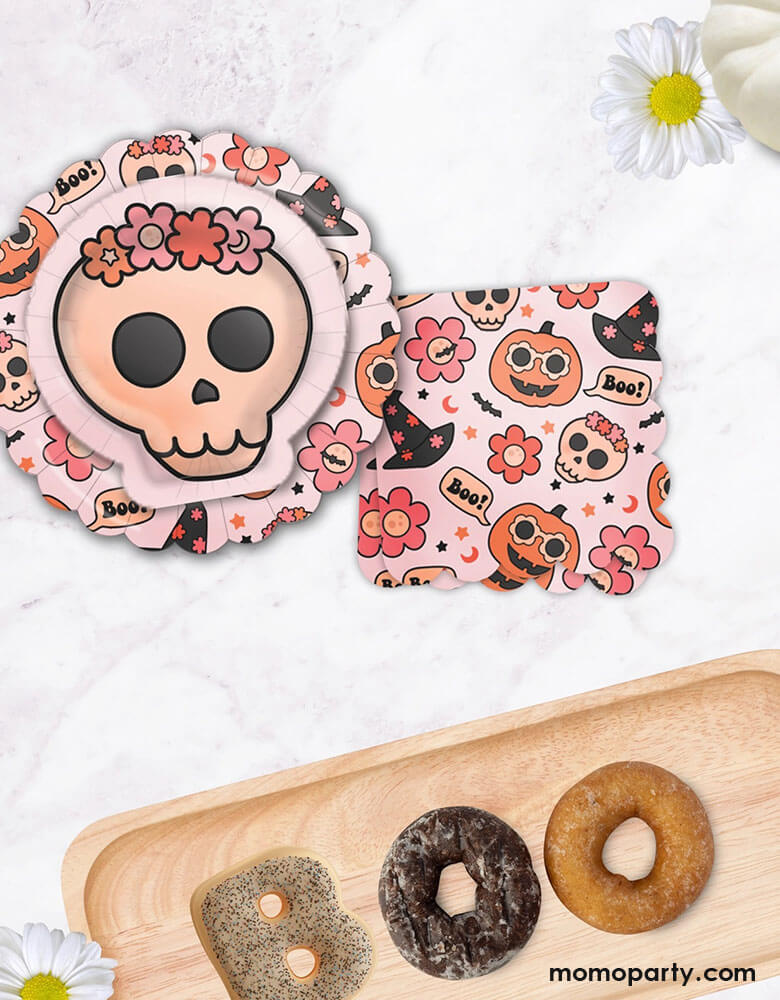 A fall Halloween party table featuring Momo Party's 8" Groovy Halloween Icon Plates, Floral skull plates and 6.5" Groovy Halloween Napkins by Ellie's Party. Next to it are some donuts shaped as "BOO" for some Halloween spooky fun. This collection is perfect for a cute and stylish Halloween table setting. Featuring groovy pumpkins, skulls, flowers, and witch hats, this party collection is great for a pink Halloween bash or kid's boho Halloween birthday party!