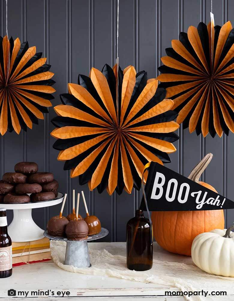 A classic orange and black Halloween table decorated with pumpkins, caramel apples and Momo Party's 14" x 15" Boo Yah black and white felt party pennant with orange and black ribbons. In the back the wall was decorated with My Mind's Eye's oversized orange and black tissue paper fans. All makes a simply yet iconic Halloween decorating inspo this Halloween season.