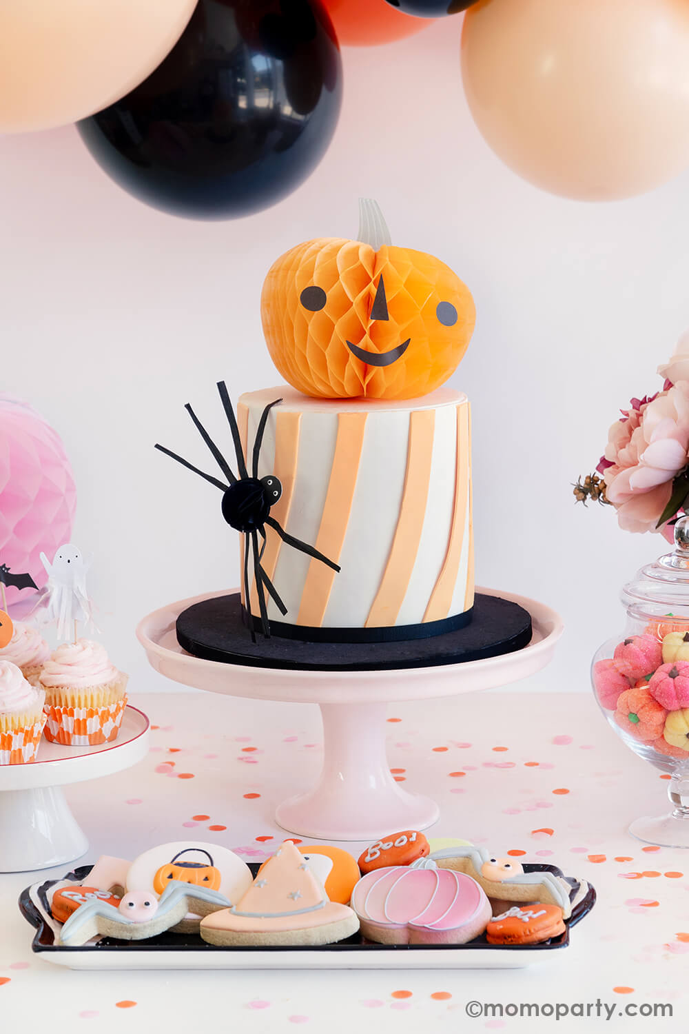 A halloween cake decorated with pumpkin honeycomb from Momo Party's Halloween Character Honeycomb set by Meri Meri. On the side of the cake, there's the small honeycomb spider. Along with pastel colored Halloween sugar cookies in the front, it makes it great Halloween treat ideas for a kid's friendly, not-so-scary Halloween party.