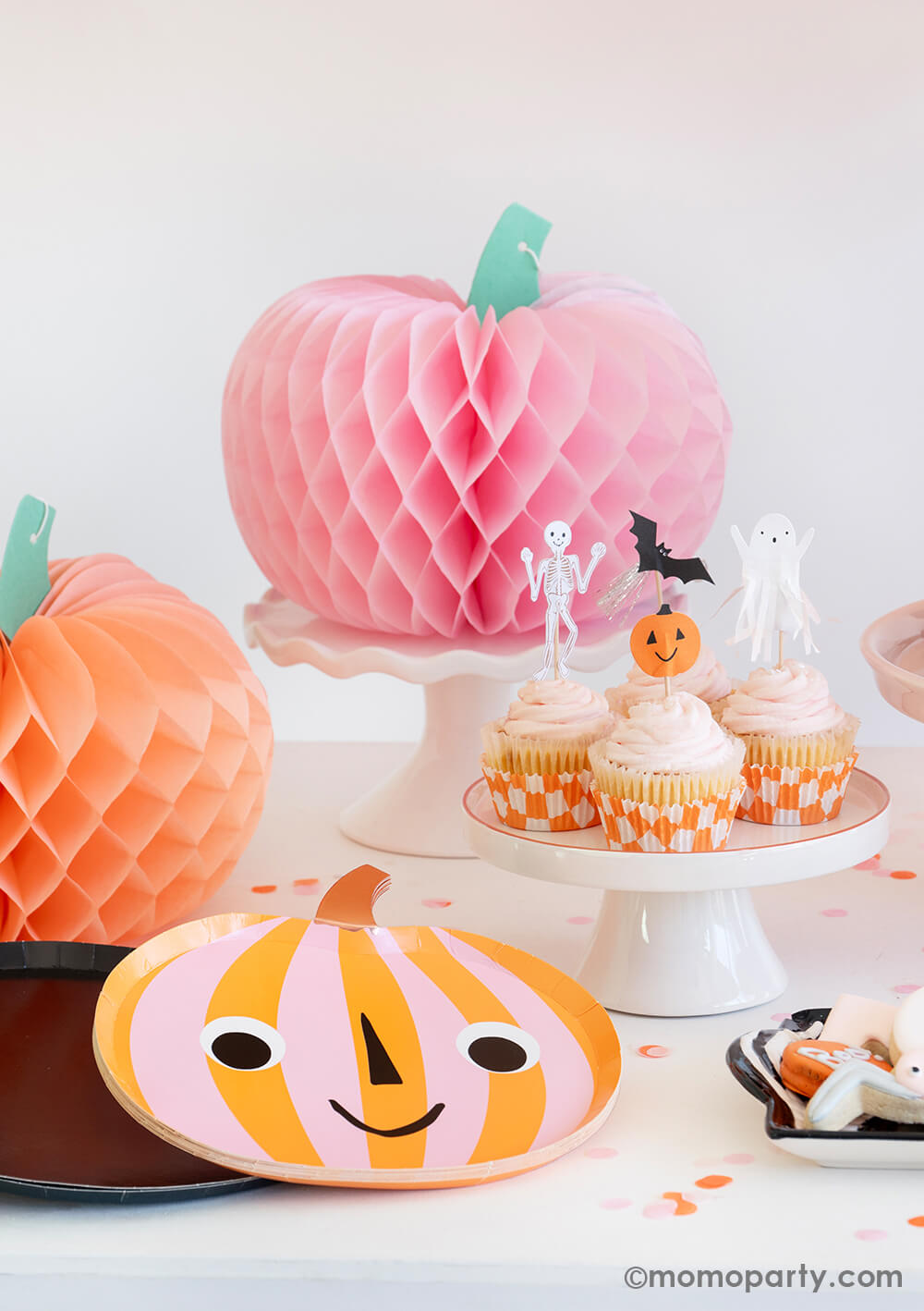 Momo Party's "Hey Pumpkin" party box featuring two honeycomb pumpkins in boo-tiful colors of pink and peach. With a smiley pumpkin shaped plates and a set of cute cupcakes topped with Halloween character toppers including a pumpkin, a skeleton, a bat and a ghost,  it creates a too cute to spook vibe for a fun kid's friendly Halloween party.