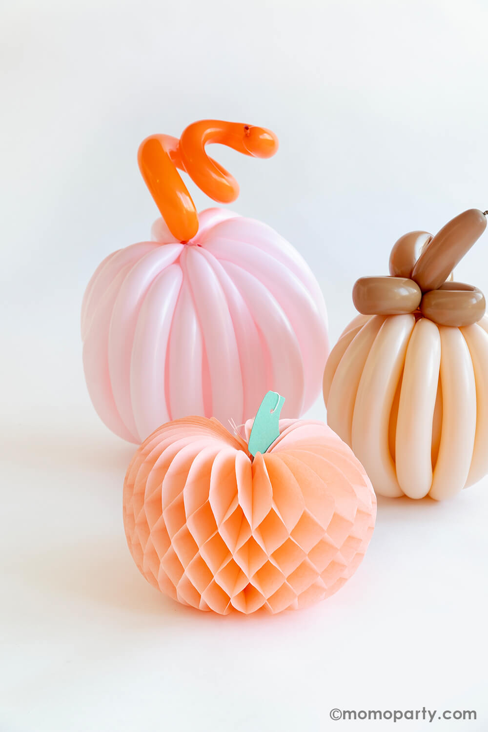 Two boho themed colored pumpkins made with twisting balloons, next to them is Momo Party's peach honeycomb decoration. All together they make a perfect fall decoration for an autumn gathering or Halloween bash.