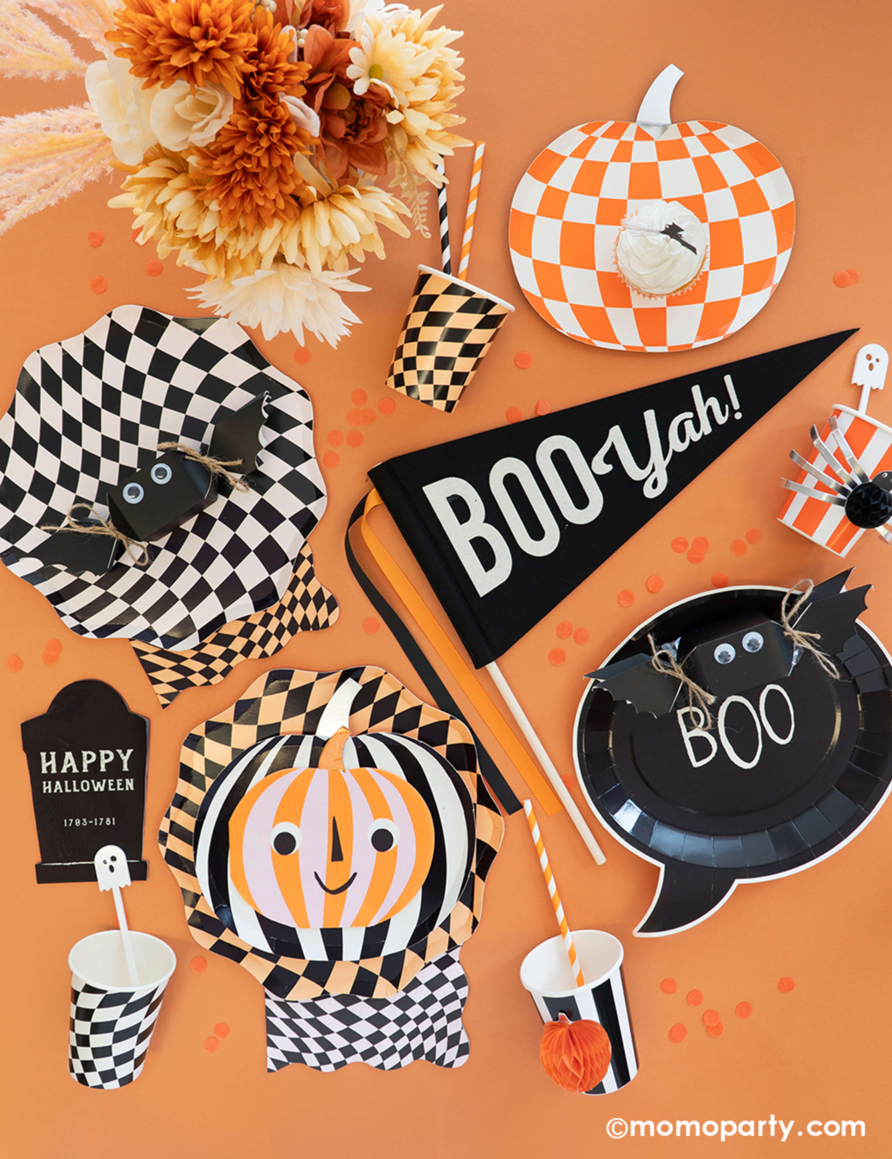 A table filled with Momo Party Classic Orange and Black Halloween Party Decorations including swirling checkered plates, cups, napkins, orange and striped pumpkin shaped plates with googly eyes, black Happy Halloween tombstone shaped napkins, Boo Yah party pennant, bat shaped jelly beans, and boo shaped plates, all makes a spooky yet fun decoration ideas for a Halloween bash this season.